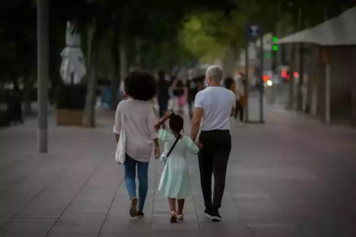 Una familia caminando de la mano por una calle arbolada al atardecer.