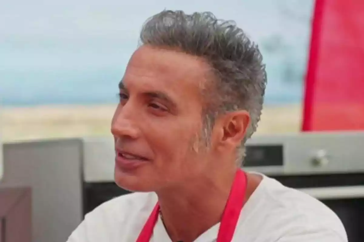 Pitingo con cabello canoso y corto lleva un delantal rojo mientras sonríe en un entorno al aire libre en MasterChef Celebrity.