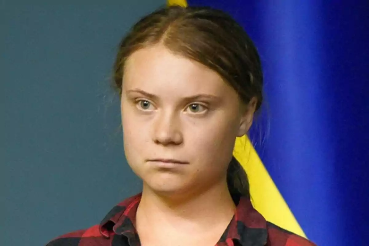 Greta Thunberg con expresión seria y cabello recogido frente a un fondo azul y amarillo. Greta Thunberg con expresión seria y cabello recogido frente a un fondo azul y amarillo.