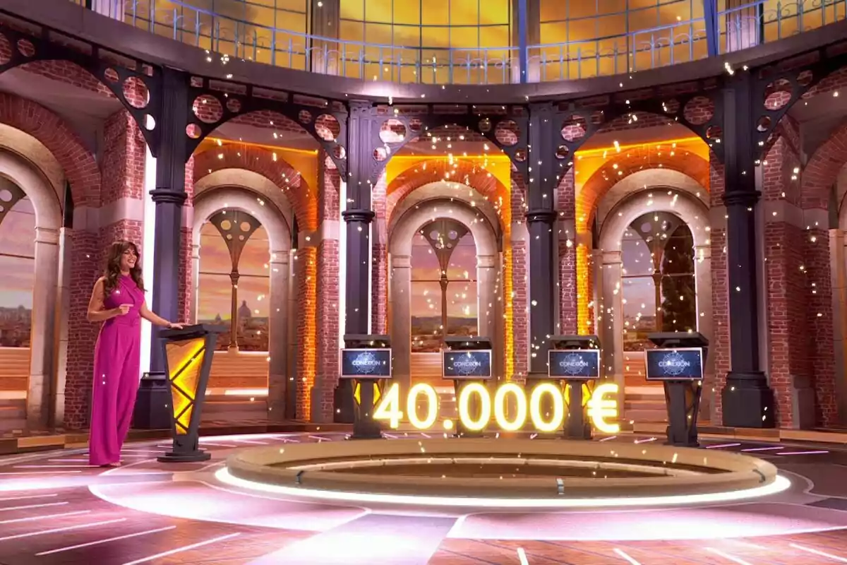 Lara Álvarez con vestido rosa está de pie en un plató de concurso iluminado con luces doradas y un premio de 40.000 euros destacado en el centro en 'La Conexión'. Lara Álvarez con vestido rosa está de pie en un plató de concurso iluminado con luces doradas y un premio de 40.000 euros destacado en el centro en 'La Conexión'.