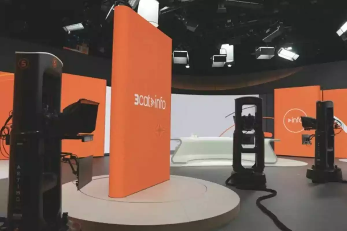 Estudio de televisión moderno del Telenotícies con cámaras profesionales y paneles naranjas con el logo de 3cat info