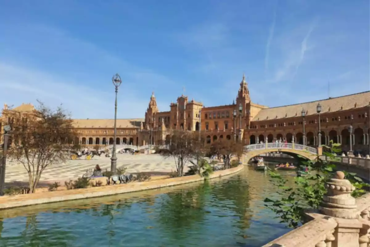 Vista de la Plaza de España en Sevilla con su arquitectura característica y un canal en primer plano bajo un cielo despejado. Vista de la Plaza de España en Sevilla con su arquitectura característica y un canal en primer plano bajo un cielo despejado.
