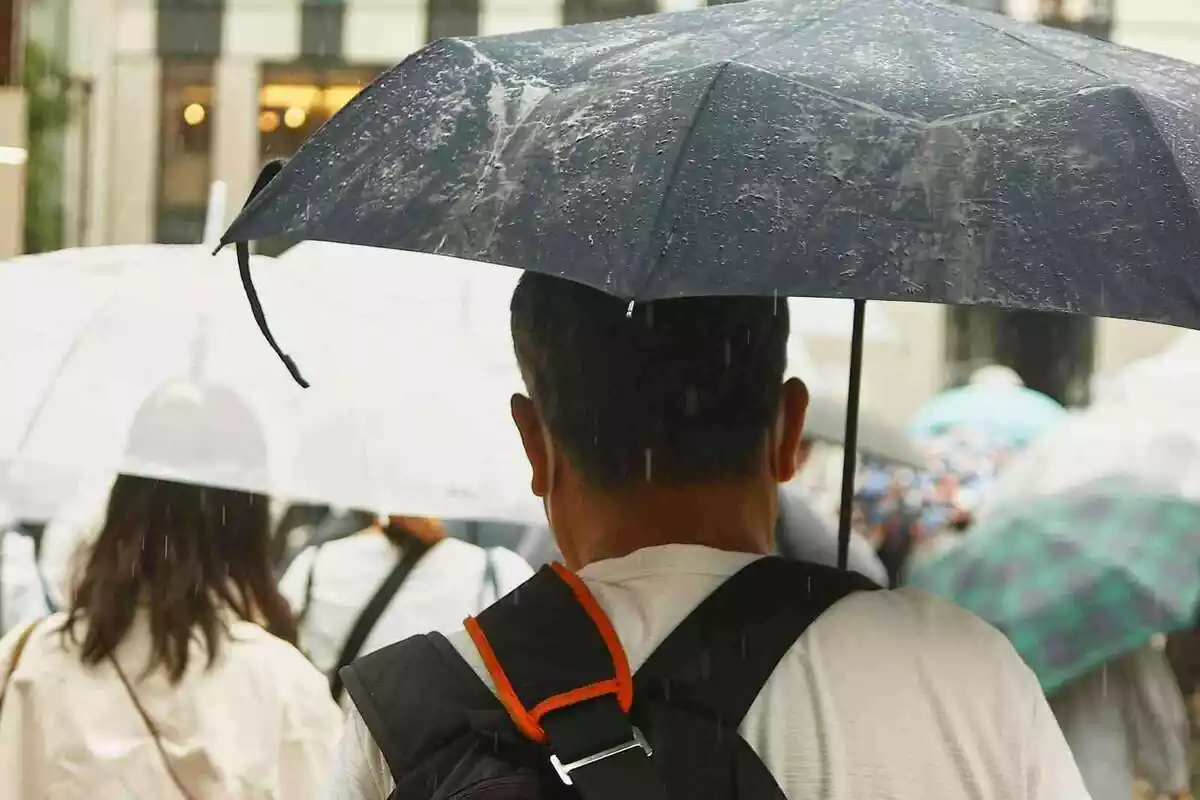 Imagen de un hombre con un paraguas escapándose de las lluvias en Barcelona