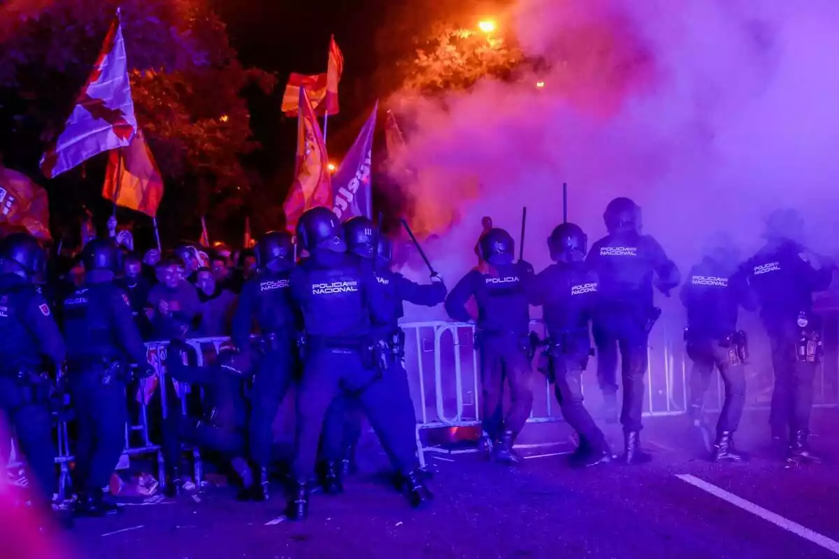 Varios policías antidisturbios intentan calmar con sus porras a los centenares de manifestantes que hay detrás de unas vallas