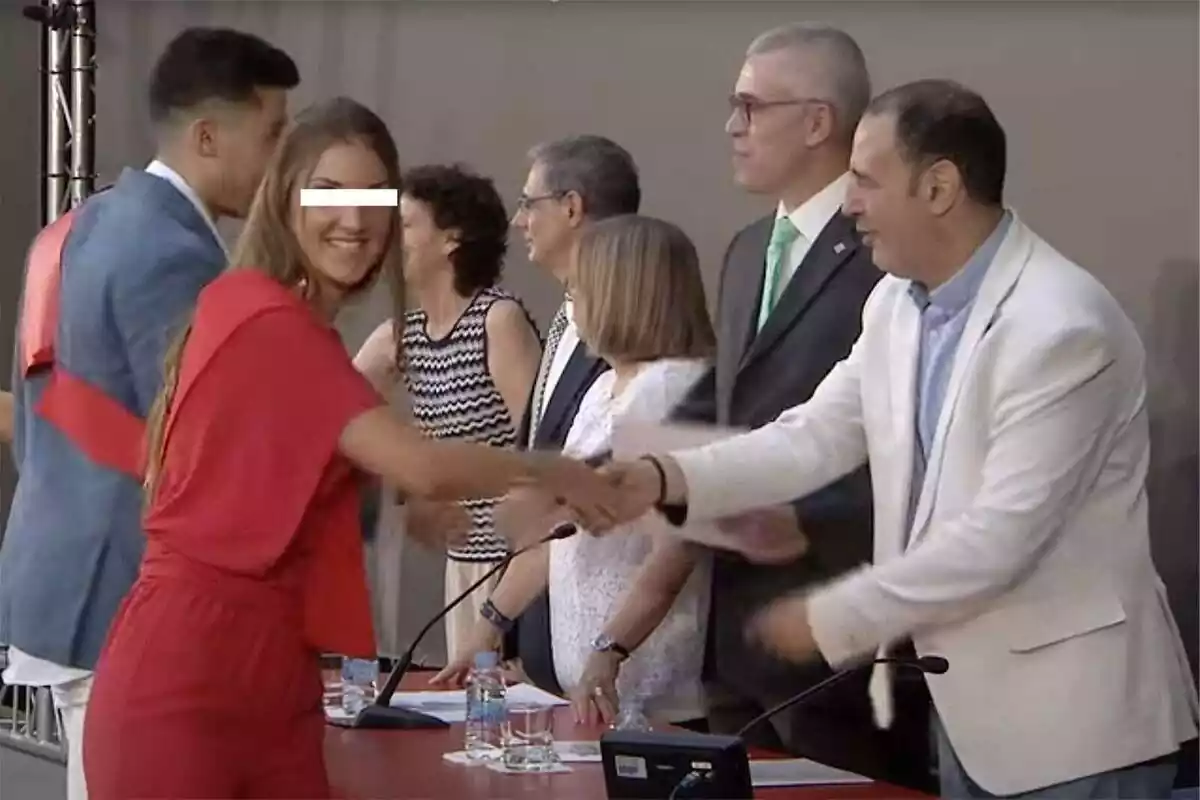 Plano americano de María, la policía infiltrada en el movimiento indepe, recogiendo su diploma de graduada mientras mira sonriente a cámera con un vestido rojo