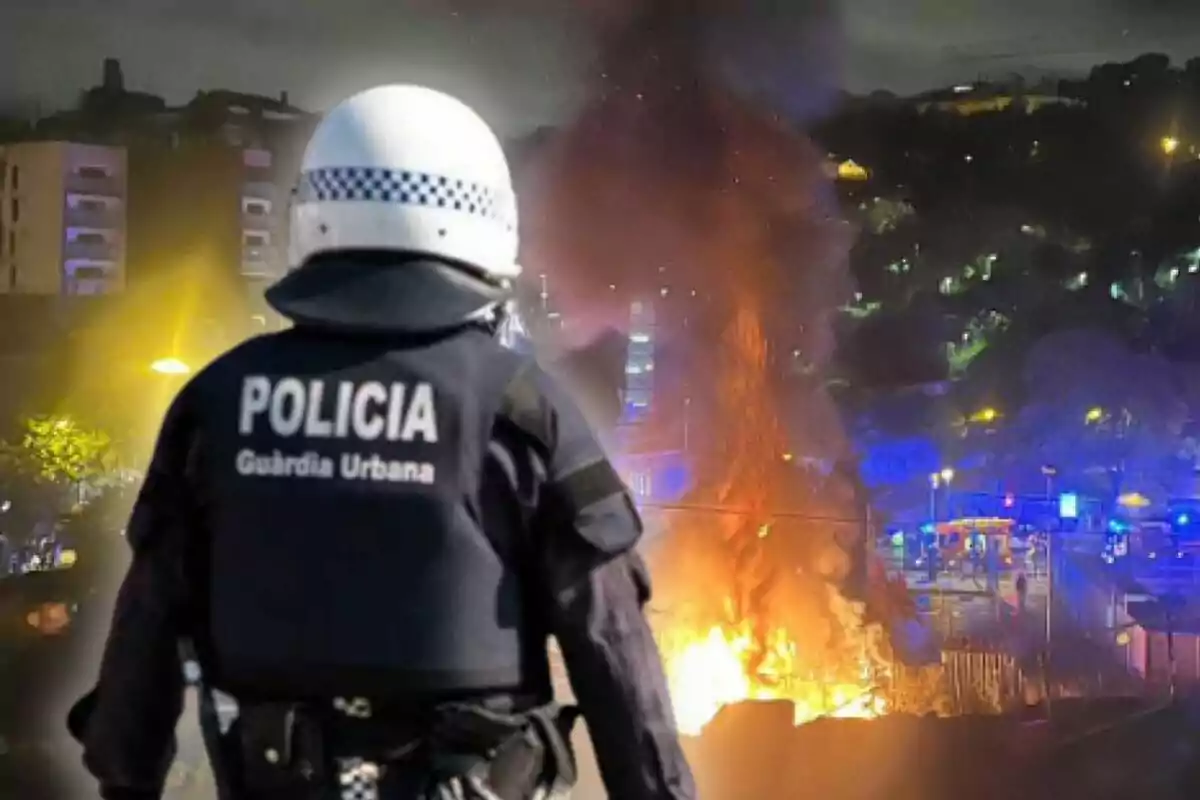 Un agente de la policía de la Guardia Urbana observa un incendio en la ciudad durante la noche, con llamas y humo elevándose en el fondo.