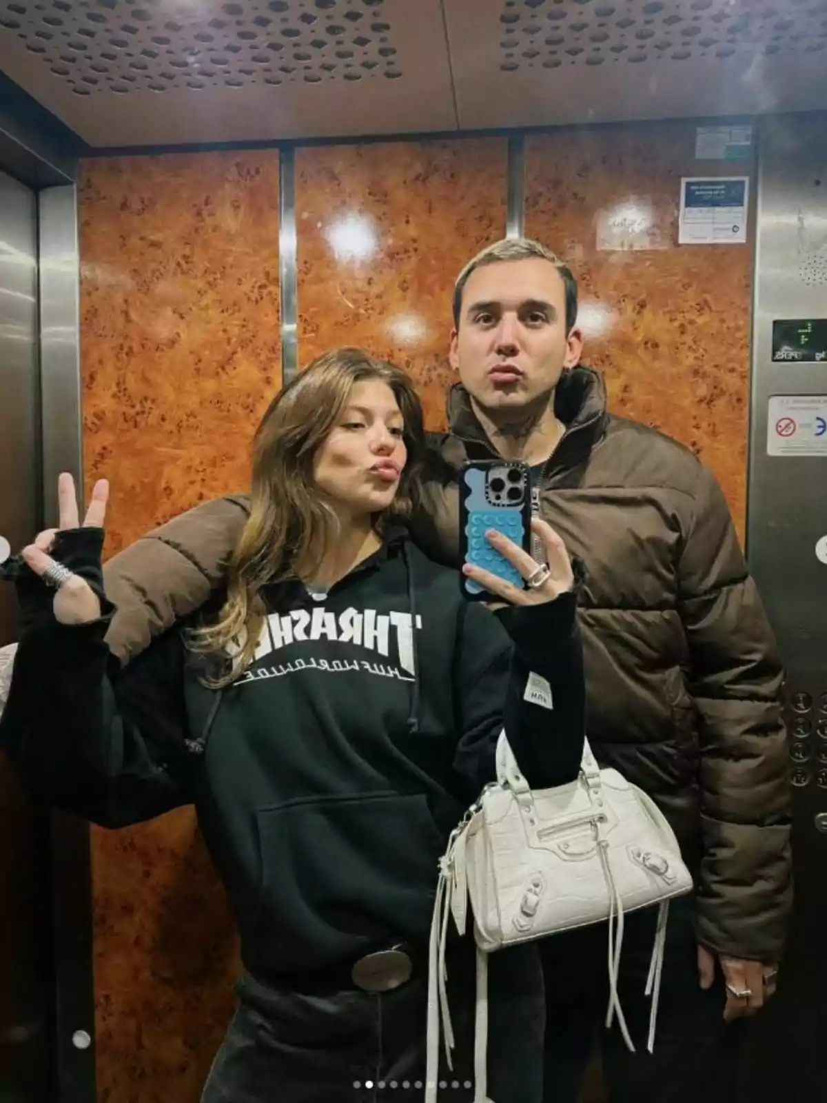 Anita Matamoros y Jhonny Garso posan para una selfie en un ascensor, una de ellas hace el signo de paz con la mano y ambas tienen expresiones divertidas. Anita Matamoros y Jhonny Garso posan para una selfie en un ascensor, una de ellas hace el signo de paz con la mano y ambas tienen expresiones divertidas.
