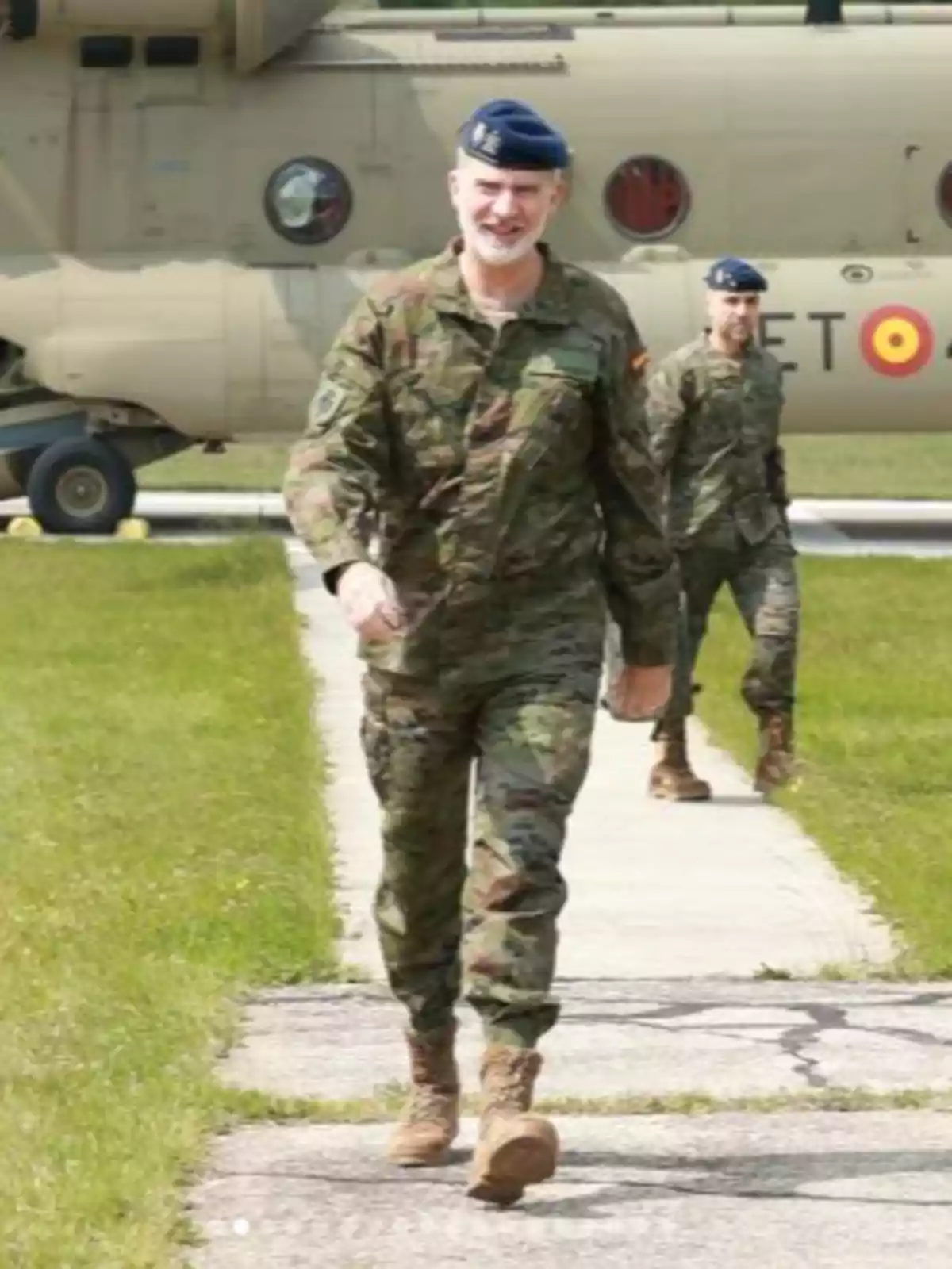 Felipe VI y otro hombre con uniforme de camuflaje y boina azul caminan por una pista de concreto con un helicóptero militar de fondo Felipe VI y otro hombre con uniforme de camuflaje y boina azul caminan por una pista de concreto con un helicóptero militar de fondo