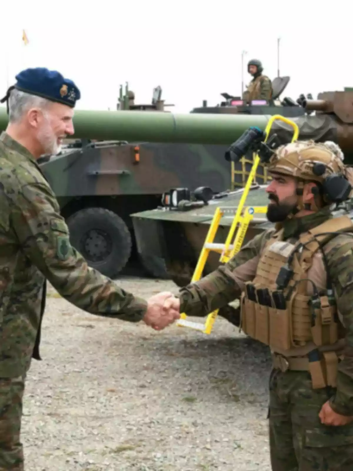 Felipe VI y otro hombre con uniforme de camuflaje se dan la mano frente a un vehículo blindado en un entorno al aire libre Felipe VI y otro hombre con uniforme de camuflaje se dan la mano frente a un vehículo blindado en un entorno al aire libre