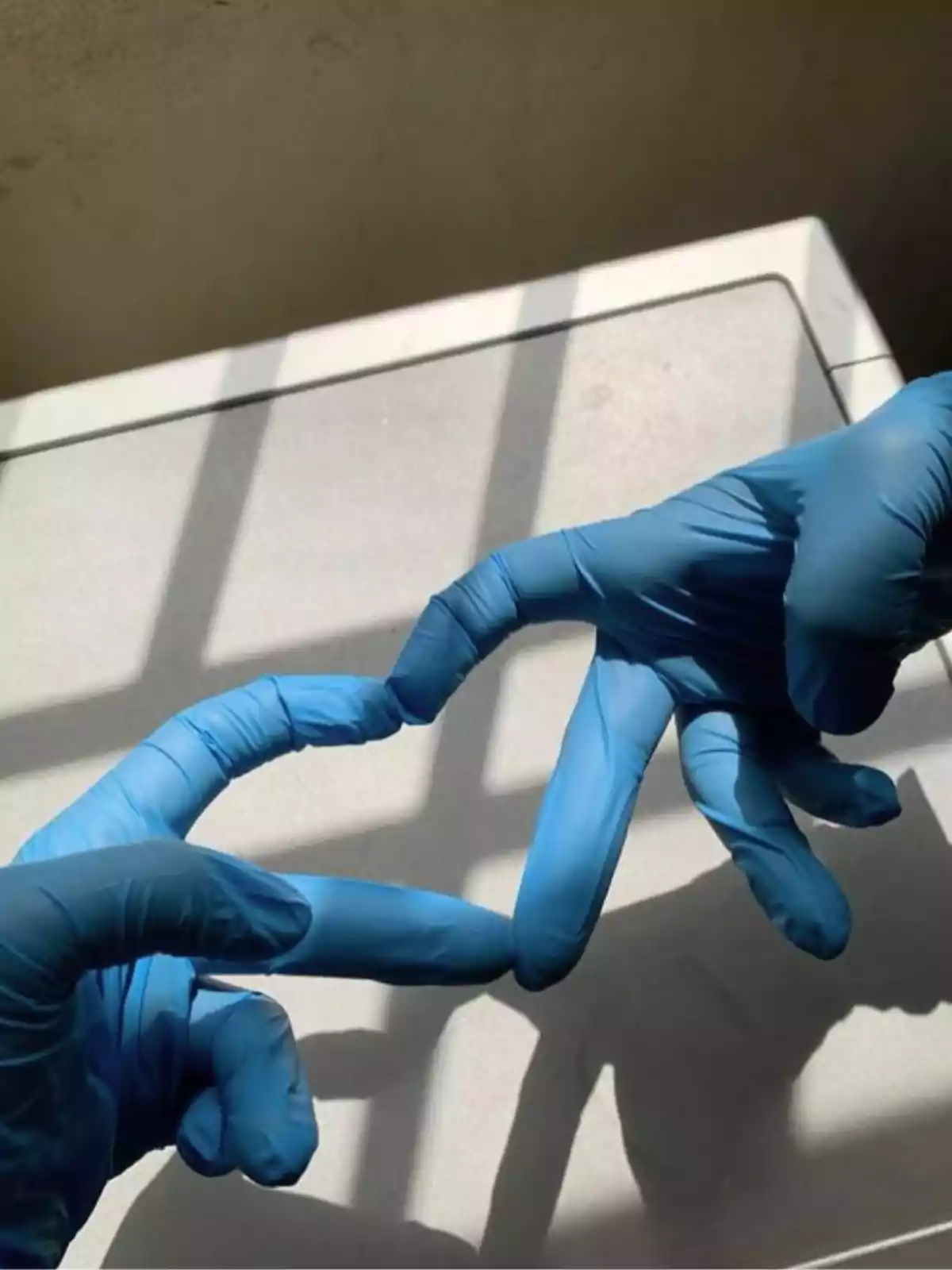 Dos manos con guantes azules tocándose con los dedos en un entorno iluminado por luz natural. Dos manos con guantes azules tocándose con los dedos en un entorno iluminado por luz natural.