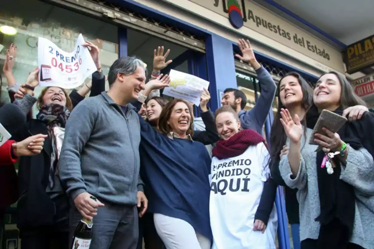 Un grupo de personas celebra con alegría frente a una administración de lotería, mostrando un cartel que indica que han ganado el segundo premio.