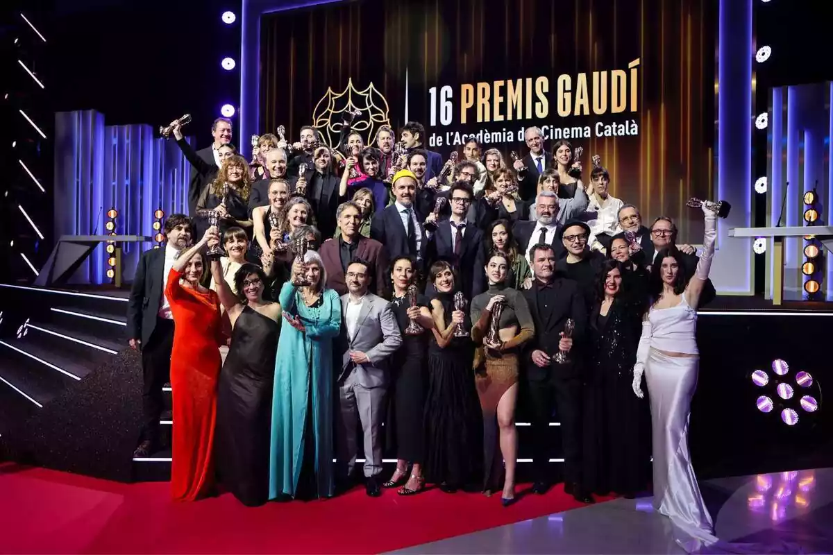 Foto de grupo con una treitena de premiados en los Premis Gaudí luciendo su trofeo en el escenario donde se celebró la gala