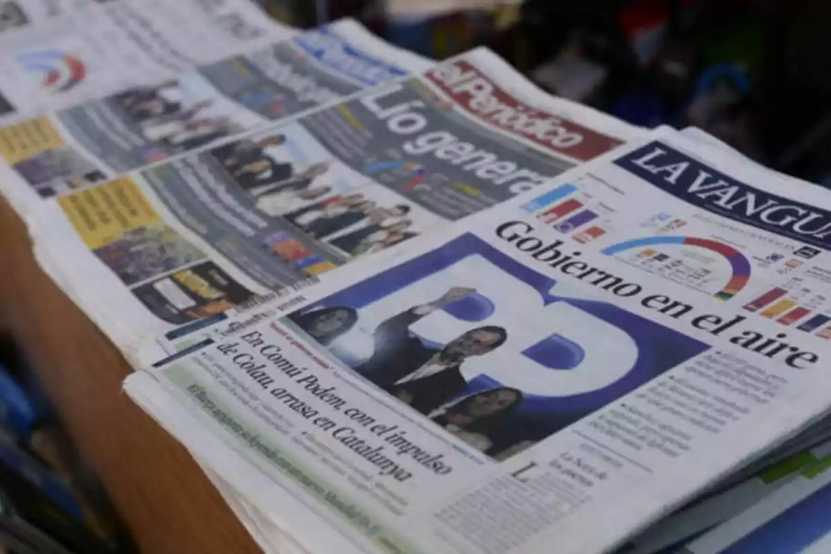 Una pila de periódicos en un quiosco con titulares visibles en las portadas.