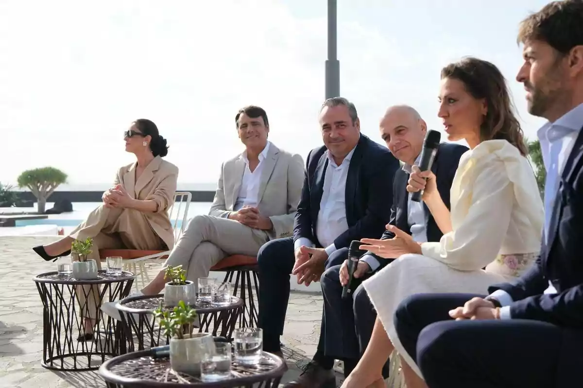 Ion Aramendi, Blanca Romero, Ángeles Blanco y Ricardo Reyes sentadas al aire libre participando en una conversación, con mesas pequeñas y plantas en primer plano.