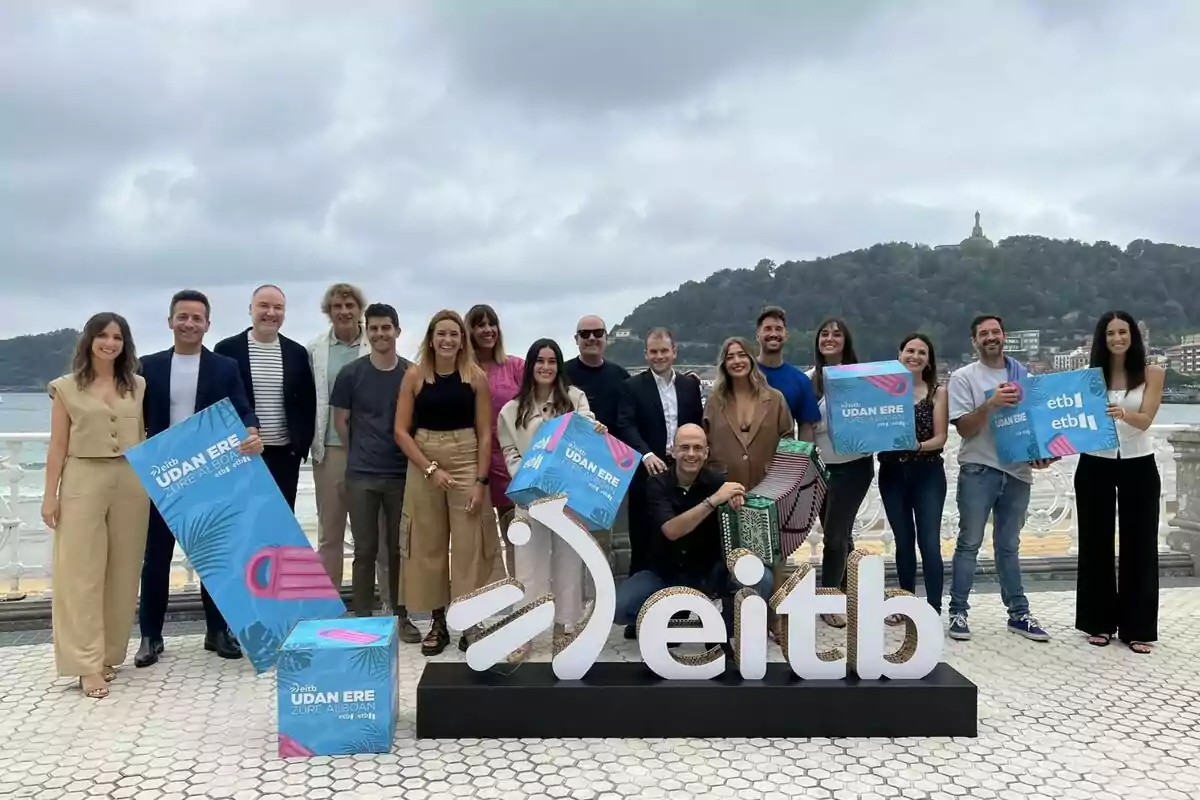 Un grupo de personas posando al aire libre junto a un cartel de eitb y sosteniendo carteles promocionales.