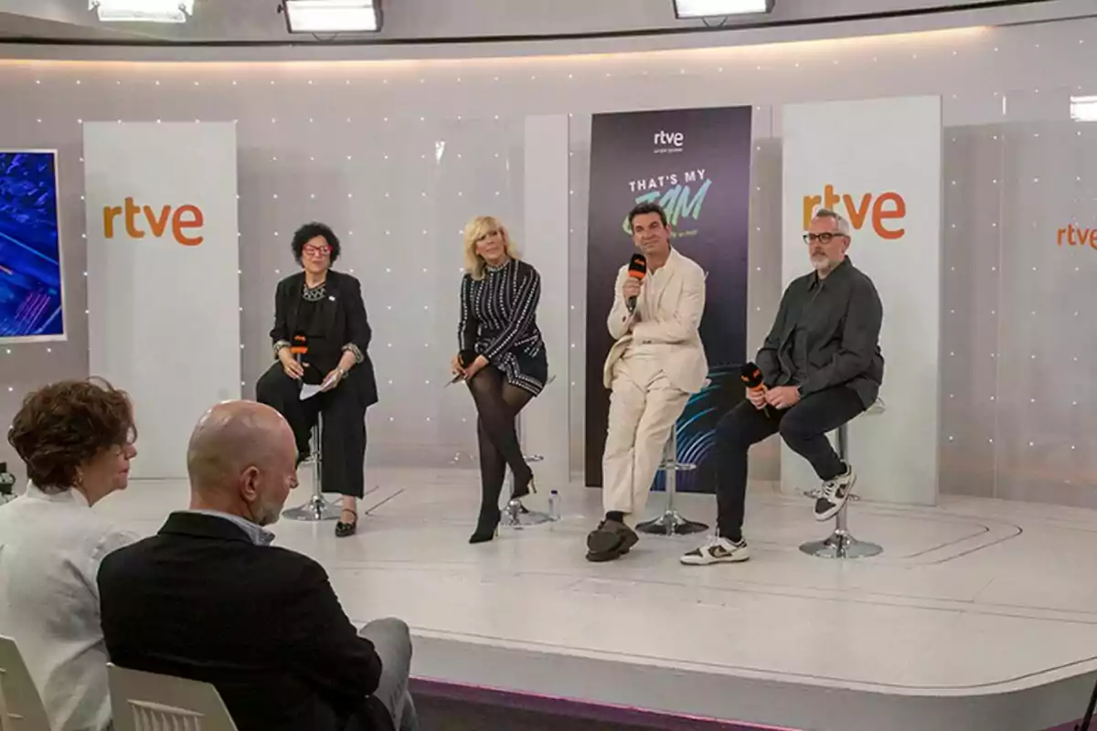 Un grupo de personas formado por Arturo Valls, Maria Eizaguirre y Miriam Corrales está sentado en taburetes en un escenario durante un evento de RTVE, con un público observando desde la audiencia en la presentación de That's my jam. Un grupo de personas formado por Arturo Valls, Maria Eizaguirre y Miriam Corrales está sentado en taburetes en un escenario durante un evento de RTVE, con un público observando desde la audiencia en la presentación de That's my jam.