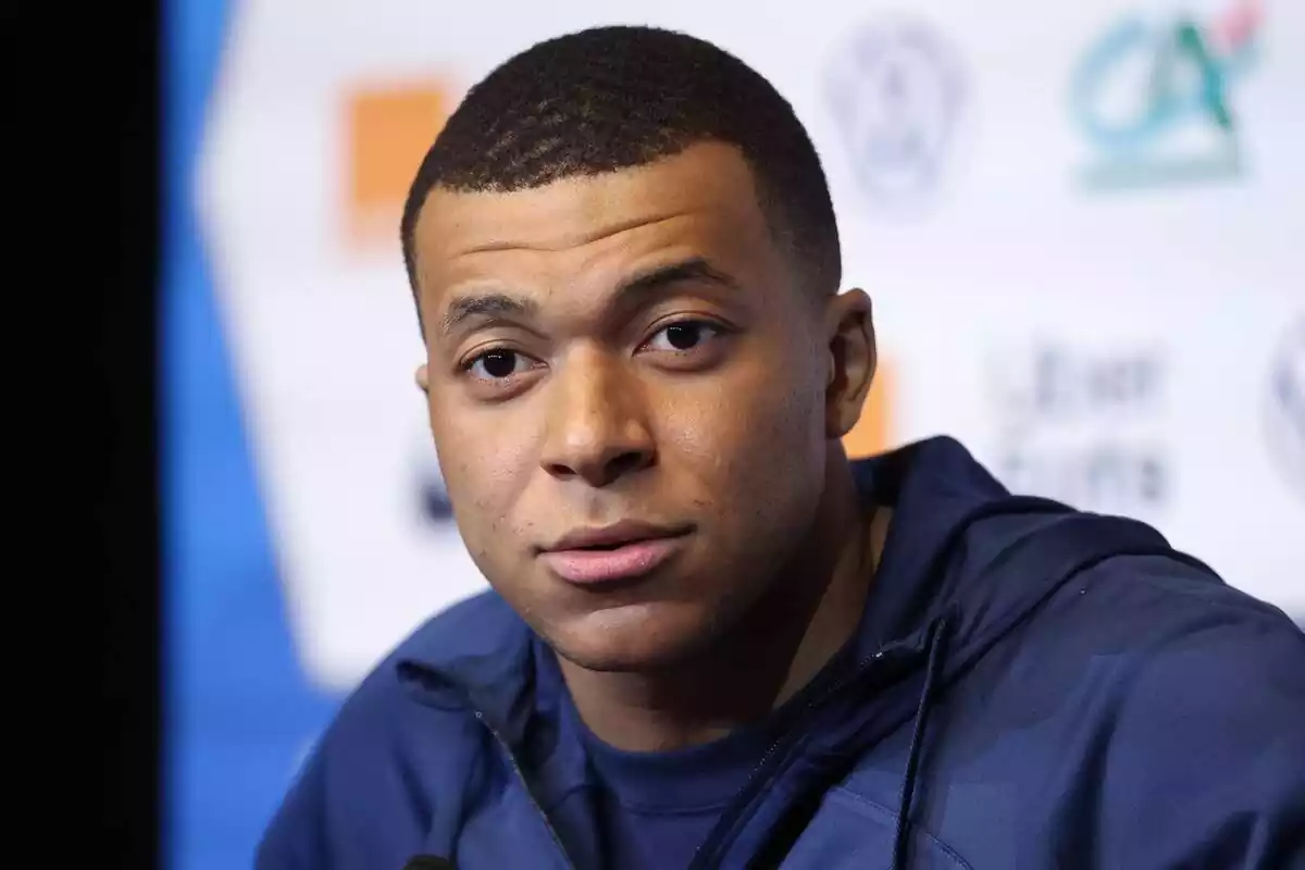 Primer plano de Kylian Mbappé con rostro neutro y una chaqueta azul