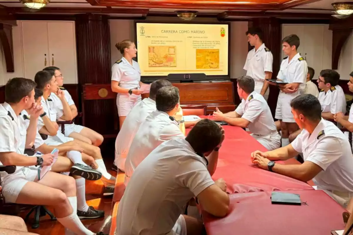 Un grupo de personas en uniforme naval asiste a una presentación en una sala con una pantalla que muestra información sobre una carrera como marino. Un grupo de personas en uniforme naval asiste a una presentación en una sala con una pantalla que muestra información sobre una carrera como marino.