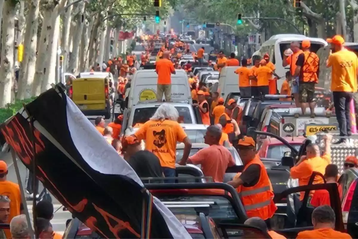 Plano general de decenas de cazadores manifestándose en Barcelona con camisetas naranjas y subidos a coches que colapsan la circulación