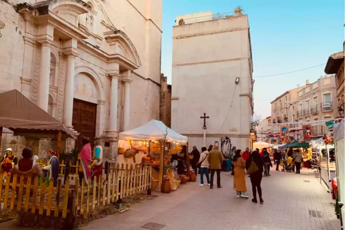 Una calle con un mercado al aire libre junto a una iglesia antigua, con personas paseando y puestos de venta iluminados.