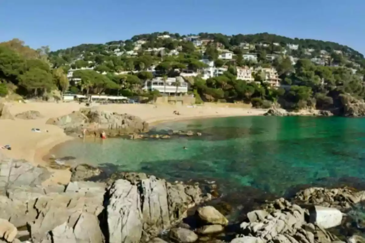 Playa con aguas cristalinas rodeada de colinas con casas y vegetación.