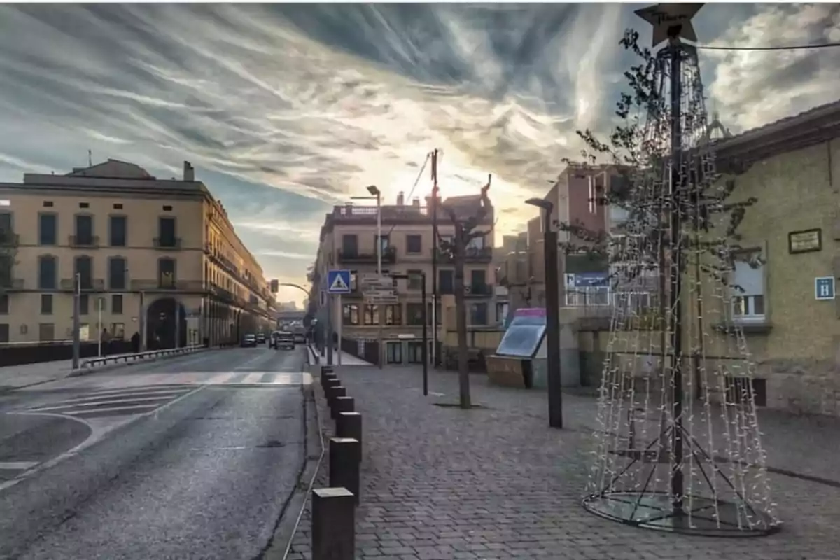 Calle urbana con edificios a los lados y un árbol de Navidad iluminado al atardecer.