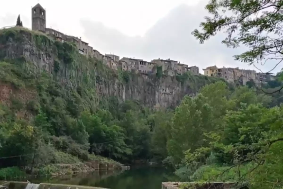 Vista de un pueblo construido sobre un acantilado rocoso con vegetación y un río en la parte inferior. Vista de un pueblo construido sobre un acantilado rocoso con vegetación y un río en la parte inferior.
