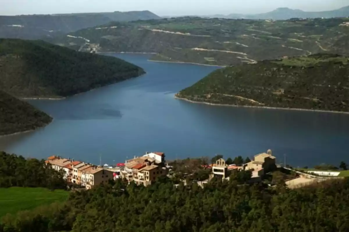 Vista panorámica de un lago rodeado de colinas verdes con un pequeño pueblo en primer plano.