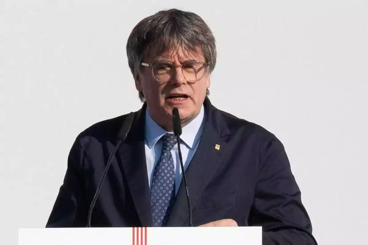 Carles Puigdemont con traje oscuro hablando en un podio con micrófonos.