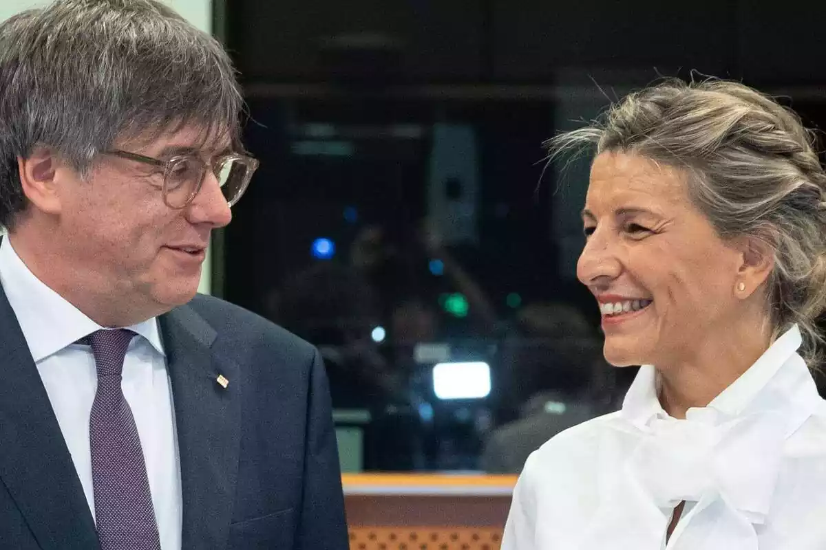 Plano medio de Carles Puigdemont y Yolanda Díaz mirándose y sonriendo