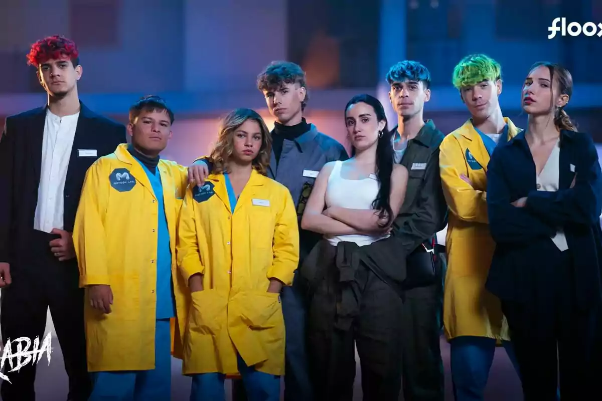 Un grupo de jóvenes posando juntos, algunos con batas amarillas y otros con ropa casual, en un ambiente iluminado, en el rodaje de Rabia.