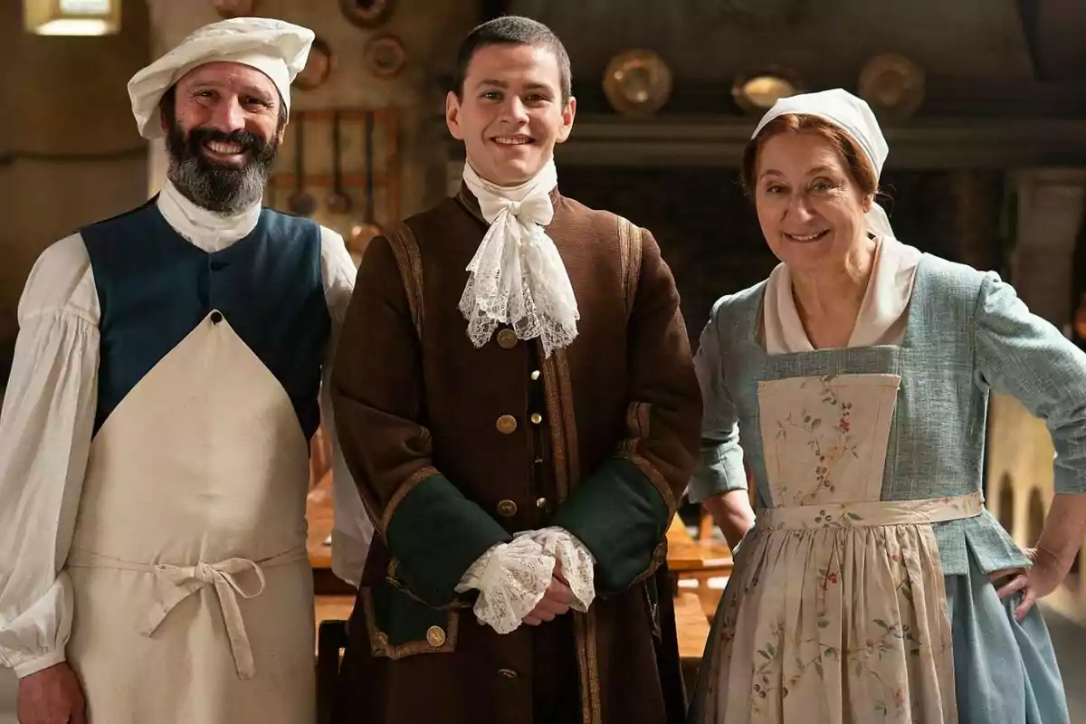 Chiqui Fernández, César Maroto y Rafa Álamos vestidas con trajes de época posan sonriendo en un ambiente que parece ser una cocina antigua en Valle Salvaje. Chiqui Fernández, César Maroto y Rafa Álamos vestidas con trajes de época posan sonriendo en un ambiente que parece ser una cocina antigua en Valle Salvaje.