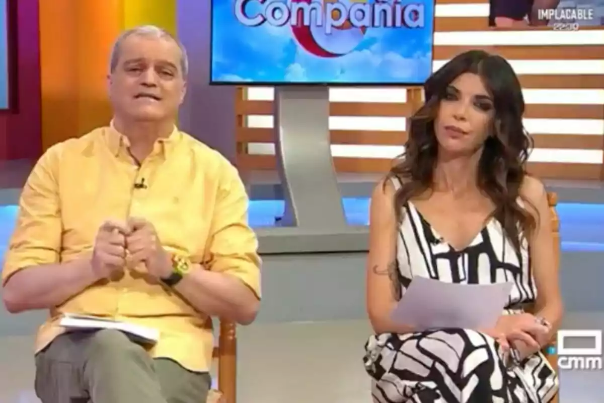Ramón García y Gloria Santoro sentados en un set de televisión colorido con un monitor al fondo que muestra el nombre del programa, 'En compañía'. Ramón García y Gloria Santoro sentados en un set de televisión colorido con un monitor al fondo que muestra el nombre del programa, 'En compañía'.