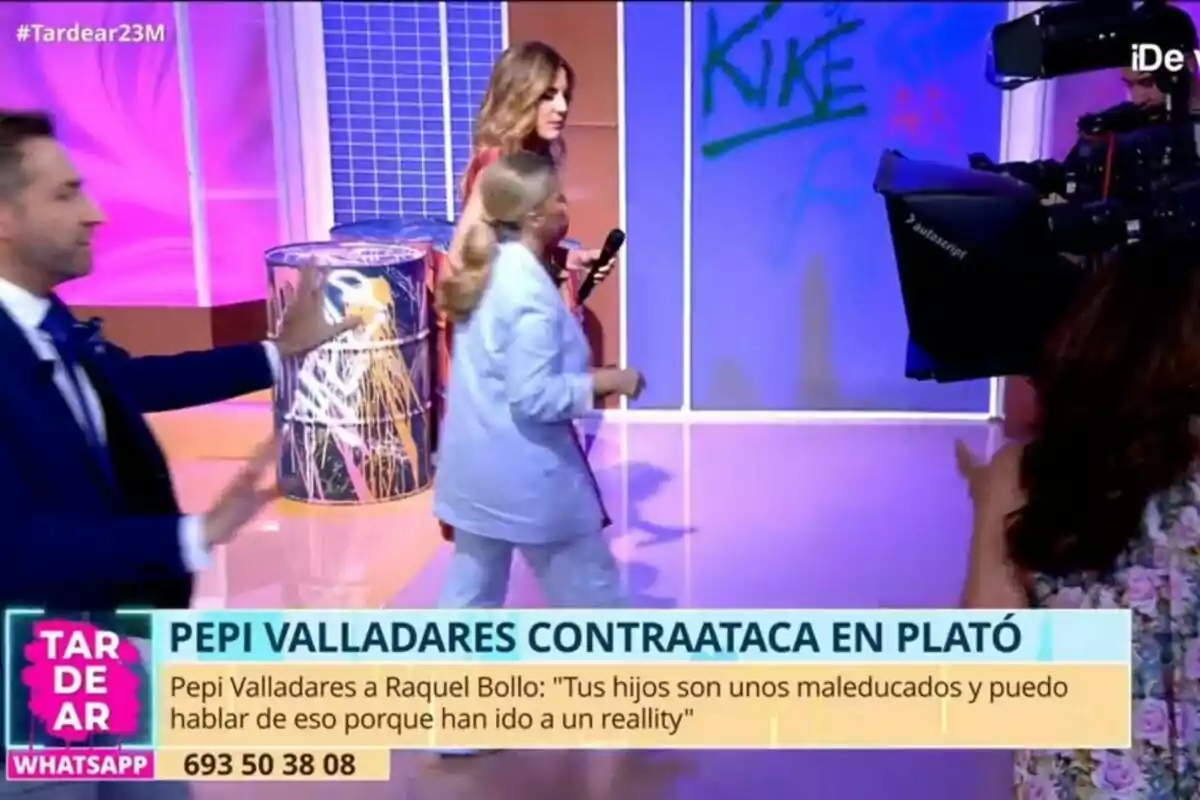 En un set de televisión de Tardear con luces de colores, varias personas interactúan mientras una cámara graba la escena. Frank Blanco con traje azul parece estar gesticulando, mientras Verónica Dulanto y Pepi Valladares caminan cerca de un barril decorativo. En la parte inferior, hay un texto que menciona un conflicto entre Pepi Valladares y Raquel Bollo. En un set de televisión de Tardear con luces de colores, varias personas interactúan mientras una cámara graba la escena. Frank Blanco con traje azul parece estar gesticulando, mientras Verónica Dulanto y Pepi Valladares caminan cerca de un barril decorativo. En la parte inferior, hay un texto que menciona un conflicto entre Pepi Valladares y Raquel Bollo.
