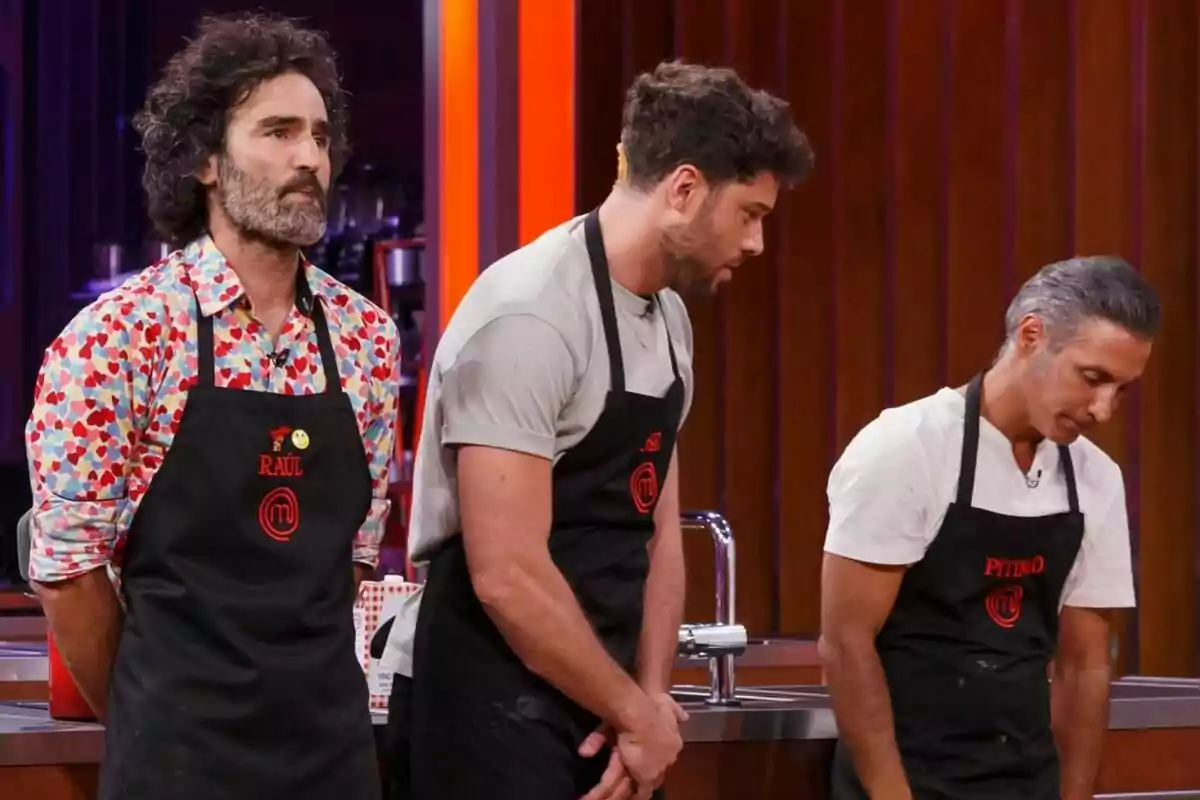 Raúl Gómez, José Lamuño y Pitingo con delantales negros están de pie en una cocina de MasterChef Celebrity.