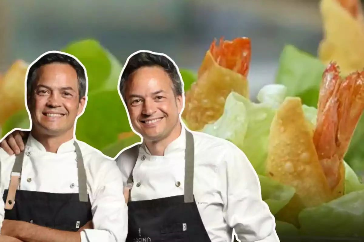 Dos chefs con delantales negros posan sonriendo frente a un fondo de comida con lechuga y camarones.