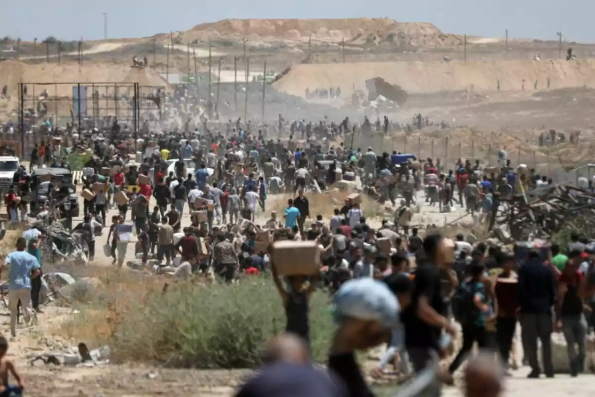 Multitud de personas caminando y cargando cajas en una zona desértica con colinas al fondo y ambiente polvoriento Multitud de personas caminando y cargando cajas en una zona desértica con colinas al fondo y ambiente polvoriento