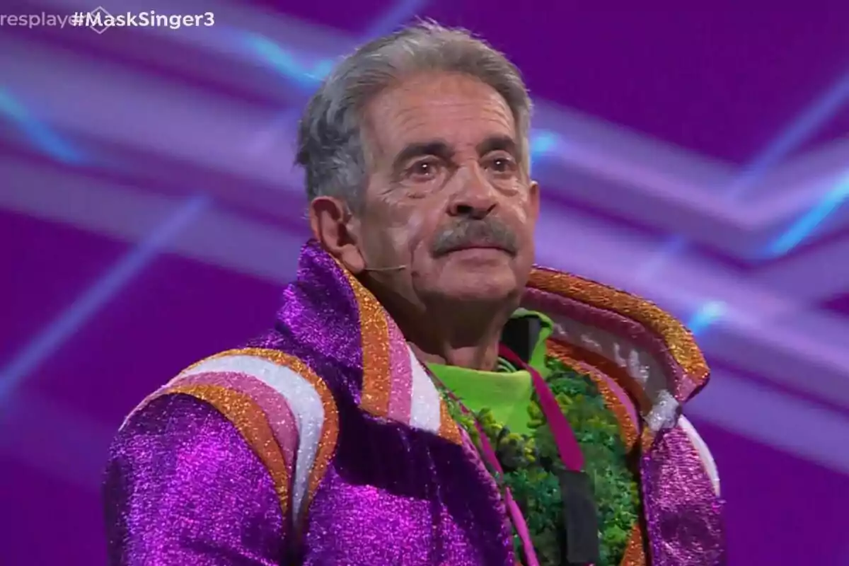 Miguel Ángel Revilla con un traje brillante y colorido en un escenario púrpura de Mask Singer.