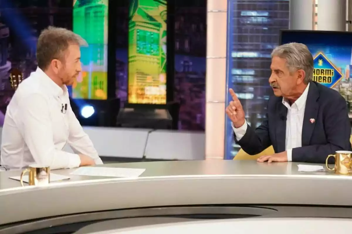 Pablo Motos y Miguel Ángel Revilla conversan en 'El Hormiguero' con decoraciones coloridas al fondo. Pablo Motos y Miguel Ángel Revilla conversan en 'El Hormiguero' con decoraciones coloridas al fondo.