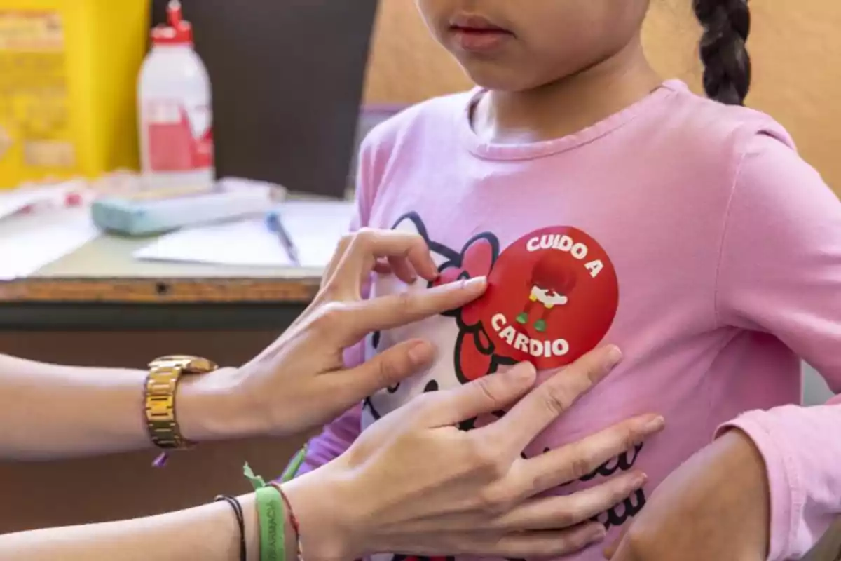 Una persona colocando una calcomanía roja en la camiseta de una niña que dice "CUIDO A CARDIO".