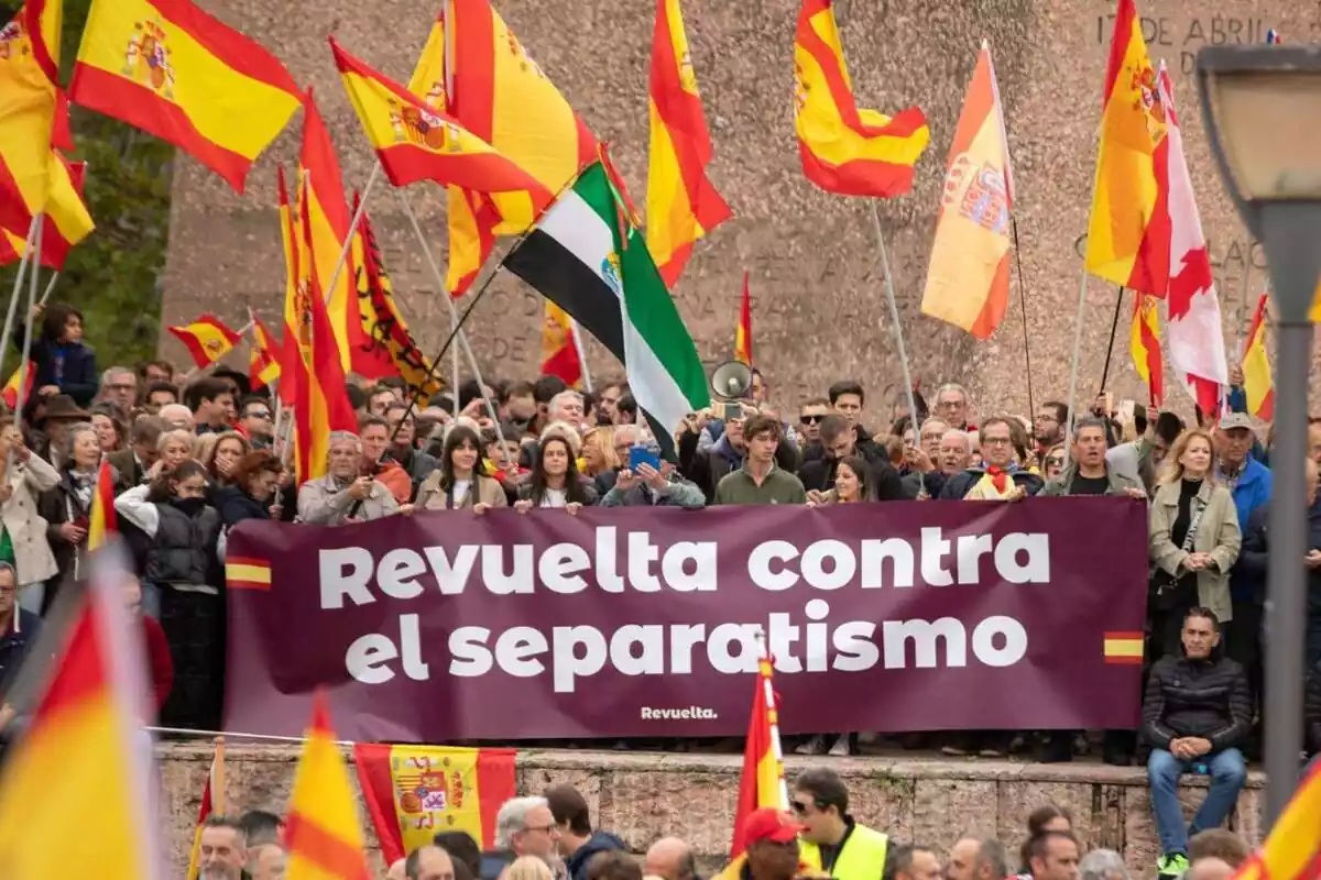 Decenas de manifestantes con banderas españolas detrás de una pancarta con el lema 'revuelta contra el separatismo'