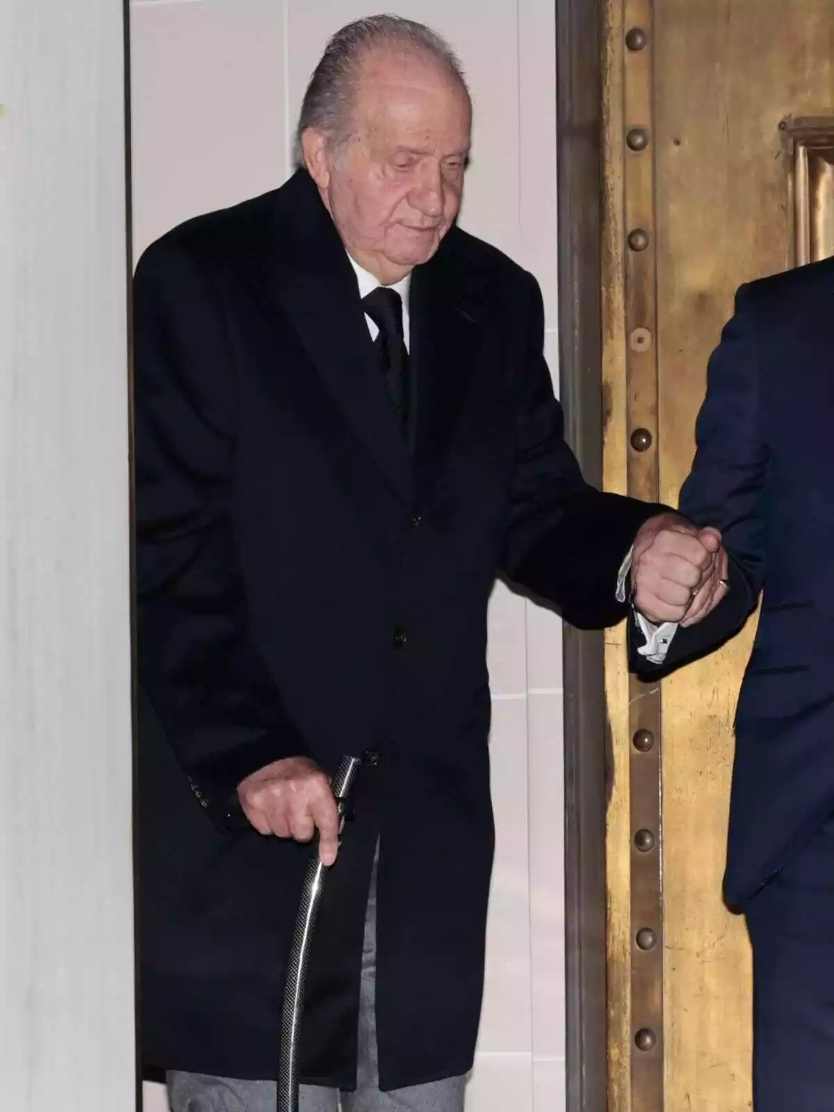 El Rey Juan Carlos I andando con la ayuda de un bastón y de un hombre