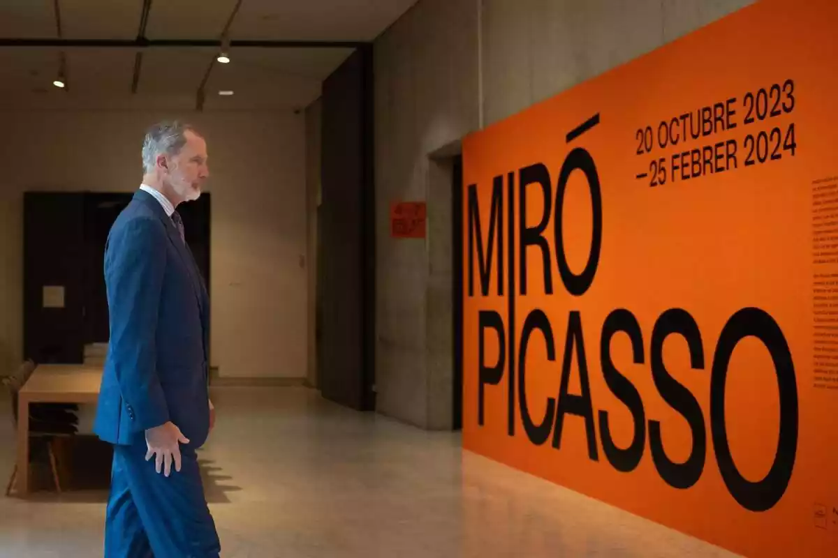 Plano americano del rey Felipe de perfil mirando un cartel naranja con los nombres de Miró y Picasso