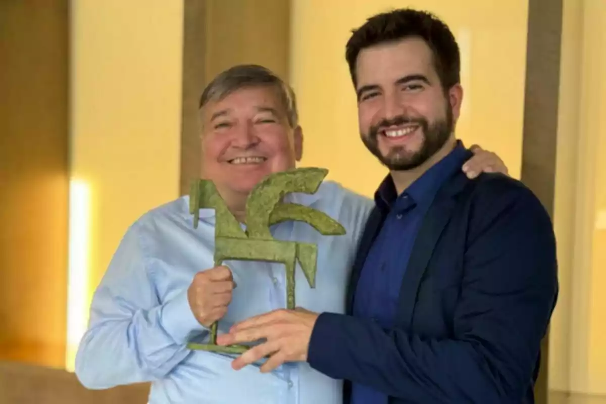 Dos personas sonrientes sostienen un trofeo en forma de caballo en un ambiente interior iluminado. Dos personas sonrientes sostienen un trofeo en forma de caballo en un ambiente interior iluminado.