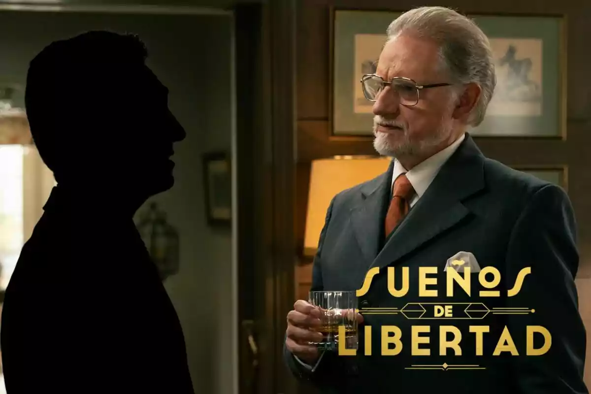 Nancho Novo con barba y gafas sostiene un vaso mientras conversa con una figura en silueta en una habitación decorada, con el texto "Sueños de Libertad" superpuesto.