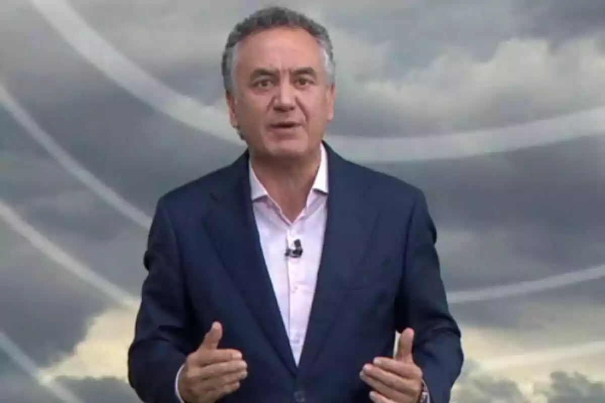 Plano medio de Roberto Brasero vestido con un traje azul y camisa clara hablando frente a un fondo de nubes grises.