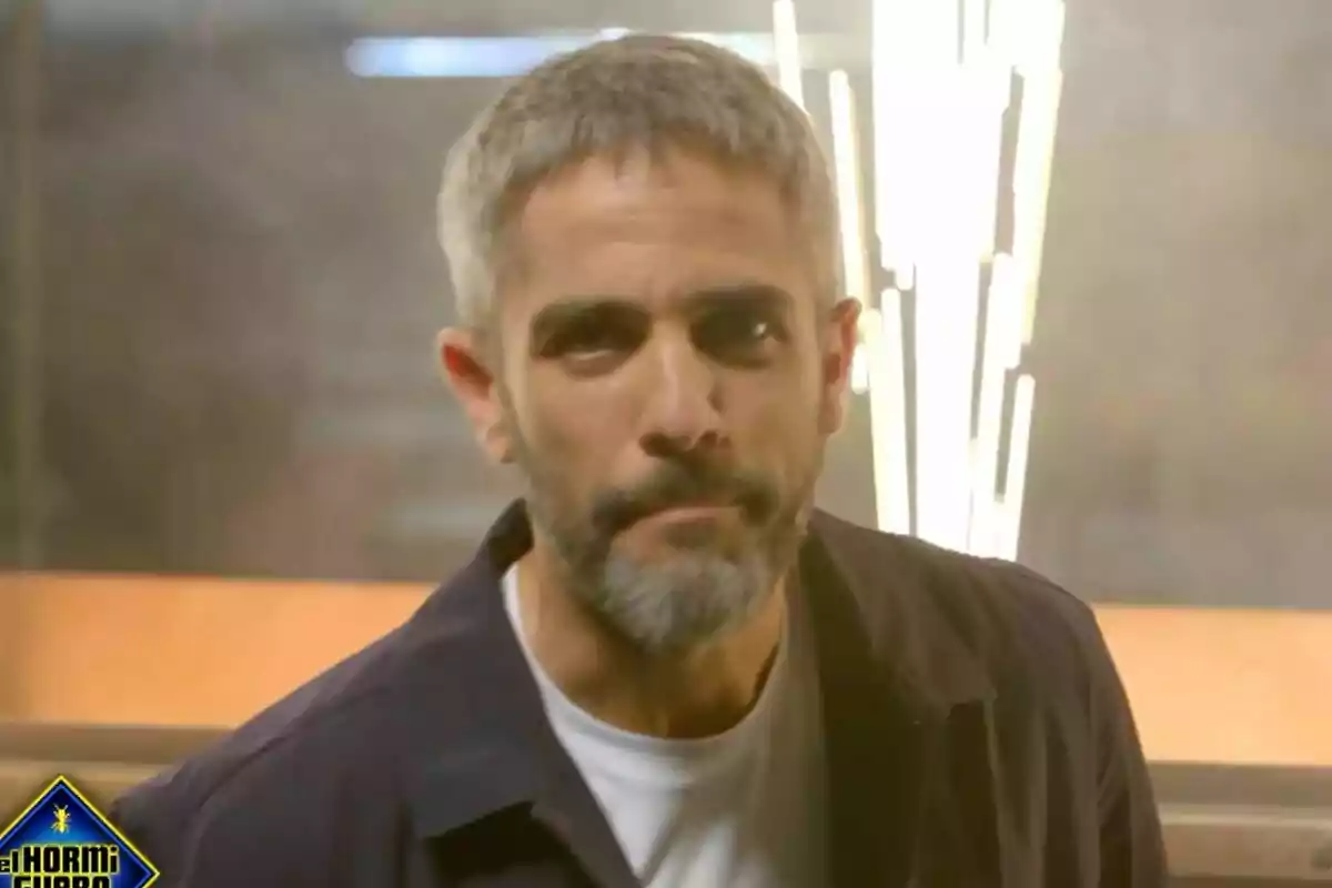 Roberto Leal de cabello corto y barba gris con expresión seria en un set de El Desafío con luces brillantes al fondo