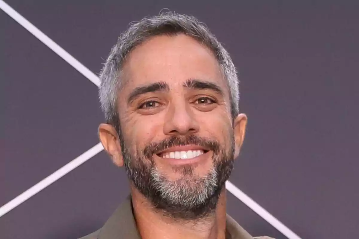 Primer plano de Roberto Leal con barba y cabello corto canoso sonriendo frente a un fondo gris con líneas blancas en la presentación de López y Leal contra el canal.