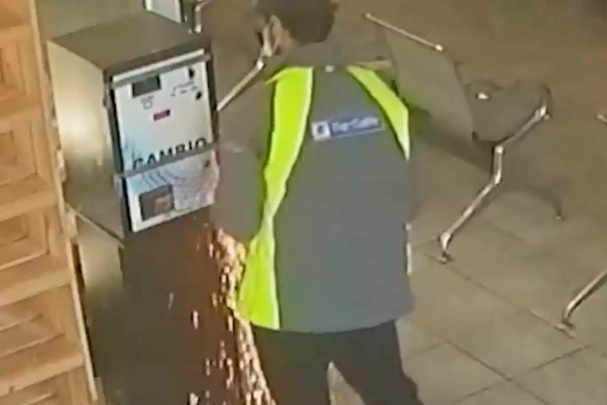 Un hombre con chaleco de alta visibilidad está usando una herramienta para abrir una máquina de cambio en un espacio interior.