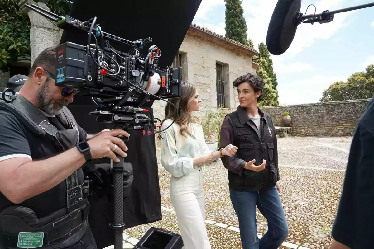 Un camarógrafo graba a Amaia Salamanca y Blanca Romero conversando en un set de filmación al aire libre en Pura Sangre. Un camarógrafo graba a Amaia Salamanca y Blanca Romero conversando en un set de filmación al aire libre en Pura Sangre.